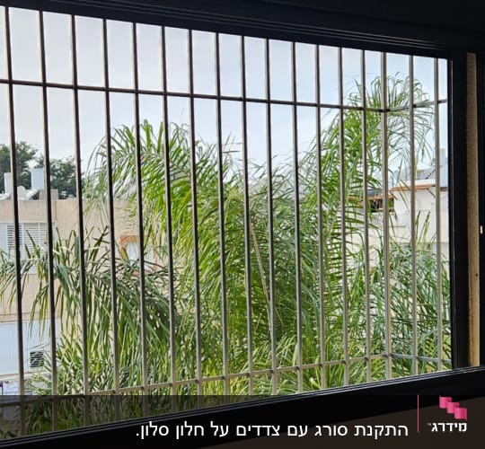 חלון עם סורגים מתכתיים ונוף של עצים בחוץ